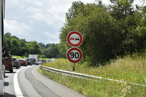 En roulant : panneaux routiers, vitesse limitée à 90 kmh, interdiction de dépasser, sur autoroute surchargée. photo