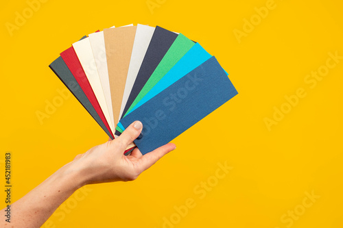 Fan of palette. Color scheme in female hands. Female hand with multi-colored cards. concept is choice of color. Fan palette in hand of designer. Multi-colored palette on yellow background. © Grispb