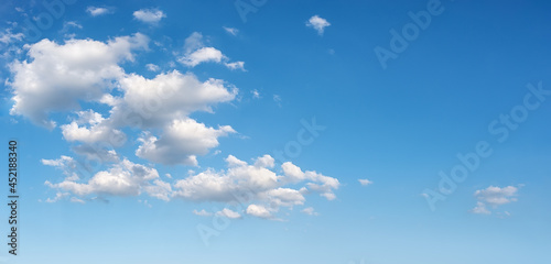 Beautiful spring sky with few white fluffy clouds on a sunny day. Clear bright blue summer sky for weather forecast, vacations and travel season ideas. Sky only panoramic image. Wide azure skyscape.
