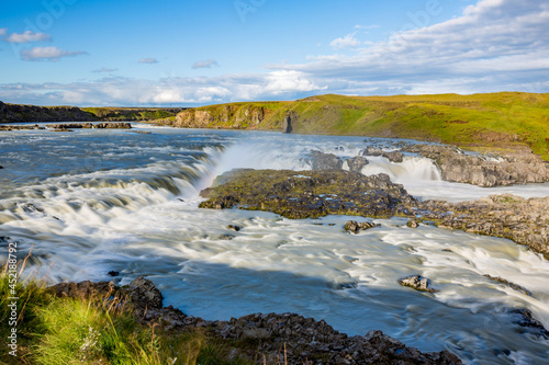 Long exposure motion blurred flow of huge river in Southern Iceland. Green hills, sunny summer day.
