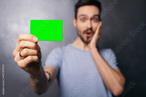 Man tattoo hold plastic discount credit card shopper beard shocked surprised european dressed plain t-shirt shopping buyings sales black friday concept copy space mock up green chromakey