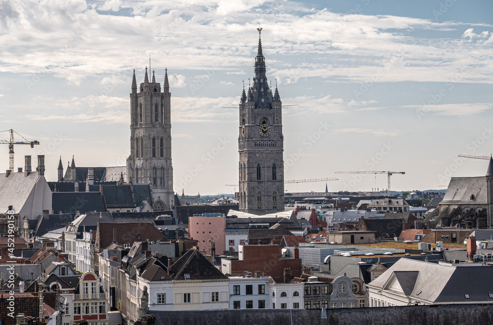 Gent, Flanders, Belgium - July 30, 2021: Aerial view on towers of Belfry with clock and Gulden Draak statue on top and Sint Baafs Cathedral under light blue cloudscape. Cityscape with gables and roofs