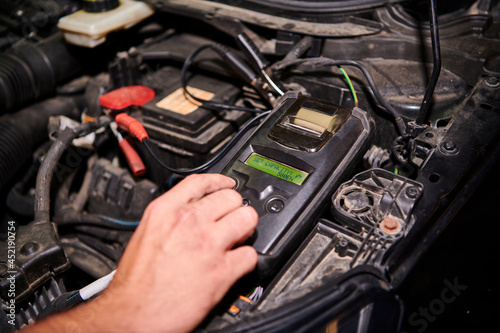 Professional Car Mechanic use  Battery Capacity Tester working in auto repair service. © Razvan