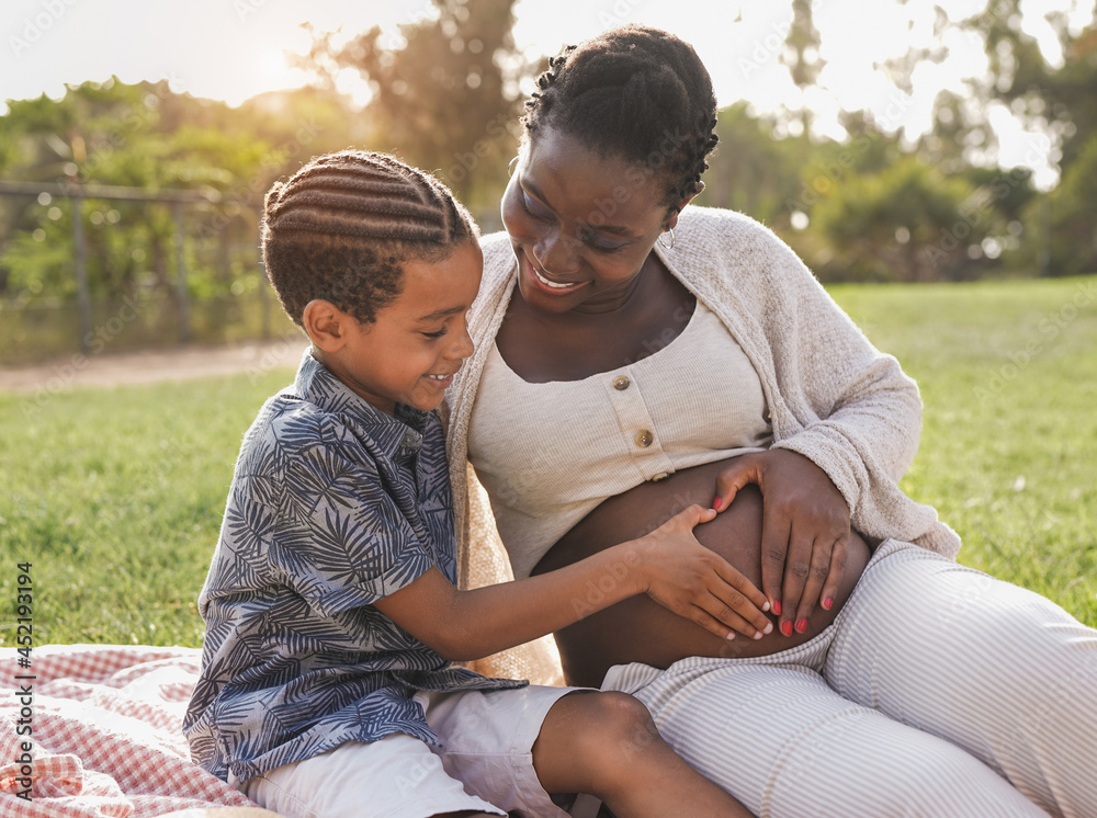 African pregnant mother and mixed race son touching belly at city park - Family love African pregnant mother and mixed race son touching belly at city park - Family love