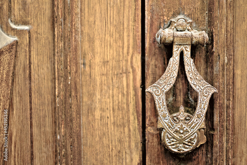 Ornate metal door knocker, old wooden door, empty space on the left. photo