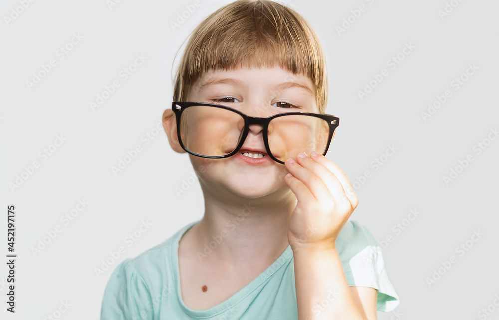 A cheerful little girl with glasses on her nose on a light background. A contented child with glasses. A joyful little girl with glasses smiles, feeling happy. Children's games, pampering. Soft focus A cheerful little girl with glasses on her nose on a light background. A contented child with glasses. A joyful little girl with glasses smiles, feeling happy. Children's games, pampering. Soft focus