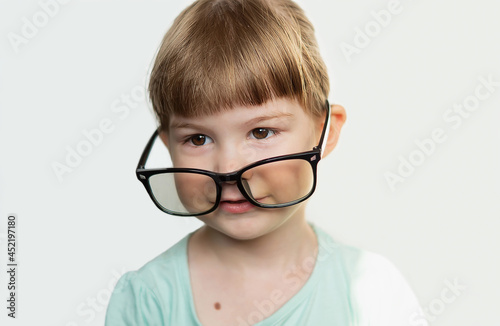 A pretty funny little girl with glasses on her nose on a light background. A contented child with glasses. A delighted little girl with glasses smiles, feeling happy. Children's games. Soft focus