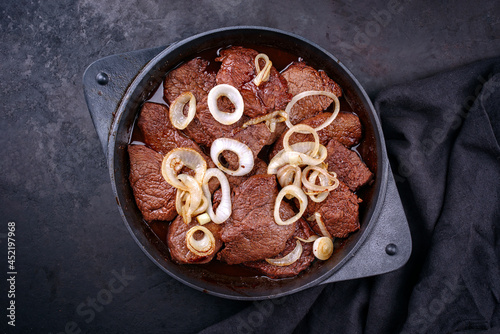 Traditional Filipino dry aged angus bistek tagalog steak with onion rings in soy sauce served as top view in a cast-iron casserole