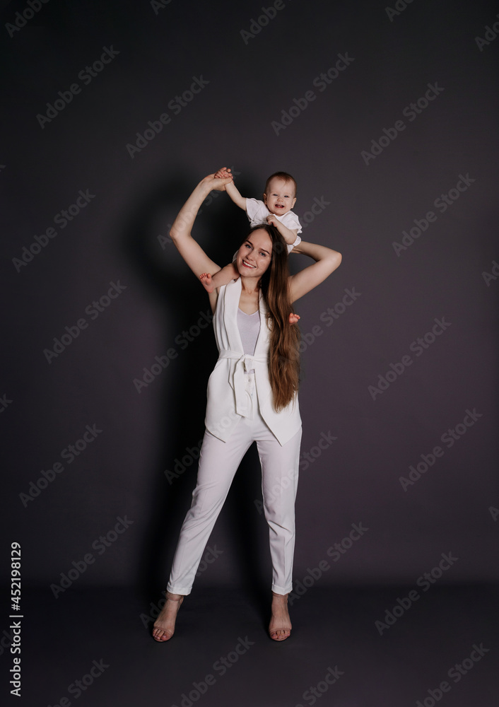 a happy mother in a white suit put a baby girl on her shoulders on a black background with a place for text