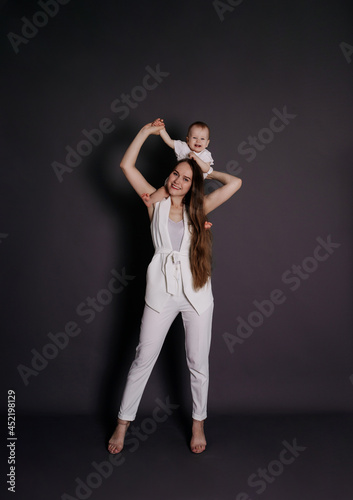 a happy mother in a white suit put a baby girl on her shoulders on a black background with a place for text