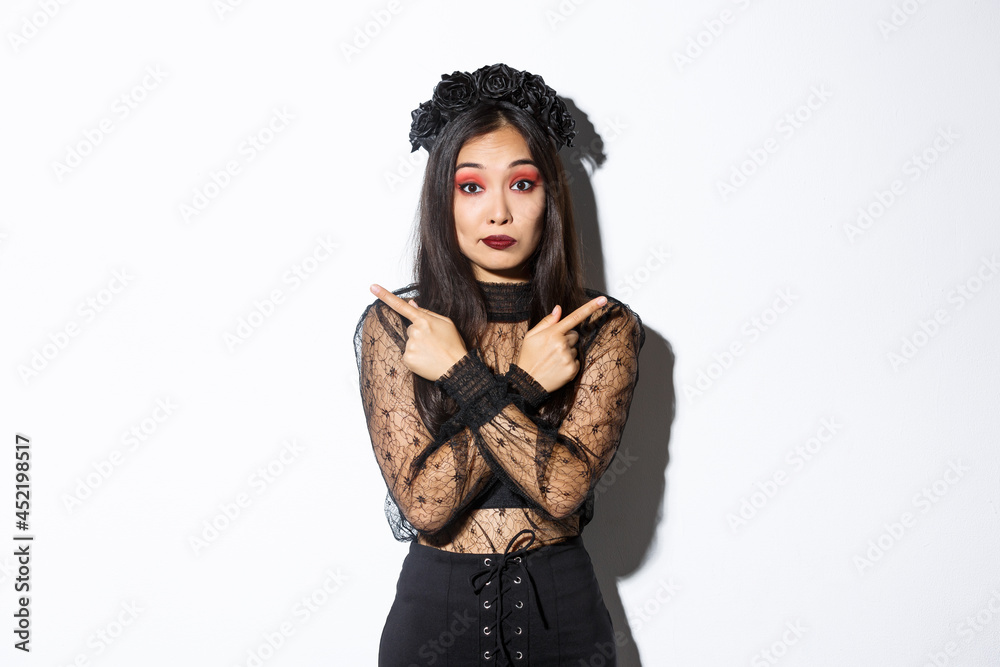 Confused pretty young woman in elegant black lace dress and wreath ...