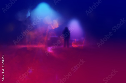 A mysterious figure standing in the middle of a road with street lights on a misty winters night. With a blurred, neon, out of focus edit © Dave