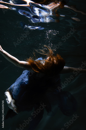 A beautiful girl in a blue dress swims underwater in the pool like a little mermaid from a fairy tale