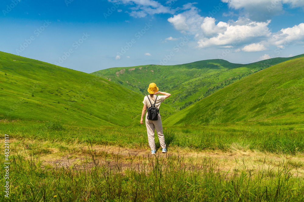 The traveler in hat and backpack resting in nature. A tourist girl looks at panorama of the mountains. Mountain beautiful landscape The traveler in hat and backpack resting in nature. A tourist girl looks at panorama of the mountains. Mountain beautiful landscape