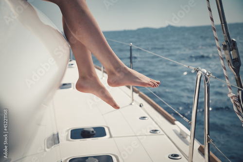 Closeup shot of young female legs with a yacht in the sea waters in the background © lo-chef