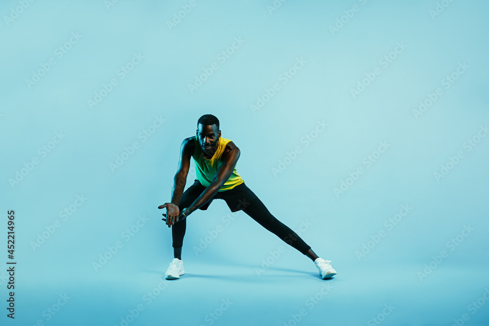 Male athlete doing stretching exercises. Young man in sports clothes warming up legs and arms.