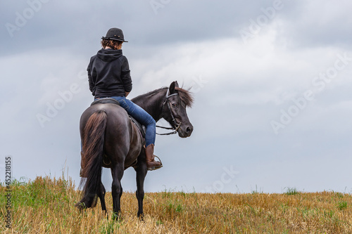 A young woman rides her horse on a stubble field; a rider on a field. Text space
