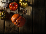 Small multi-colored pumpkins and pine cones on a wooden texture. Halloween holiday. High angle view. Postcard, invitation, banner, poster. There are no people in the photo. Color image.
