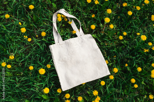 White cotton or mesh bag on dandelion grass background. Zero waste, no plastic, eco friendly shopping, recycling concept. Blank mockup shopper with place for artwork or text. Flat lay, copy space