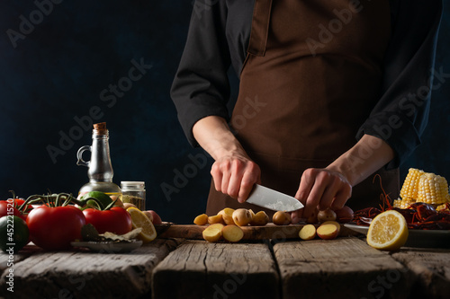 The cook prepares corn with crayfish, potatoes, lemon and other ingredients on the table. Delicious nutritious dish. Wooden texture. Restaurant, hotel, advertising.