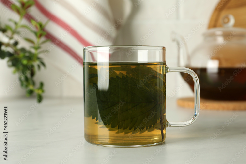 Glass cup of aromatic nettle tea on white table