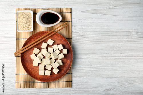 Delicious tofu with soy sauce and sesame seeds on white wooden table, flat lay. Space for text