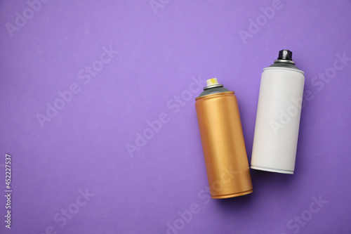 Cans of different graffiti spray paints on violet background, flat lay. Space for text