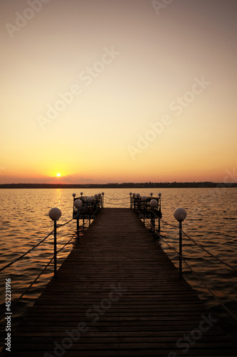 Picturesque view of empty wooden pier with lanterns at sunset © New Africa