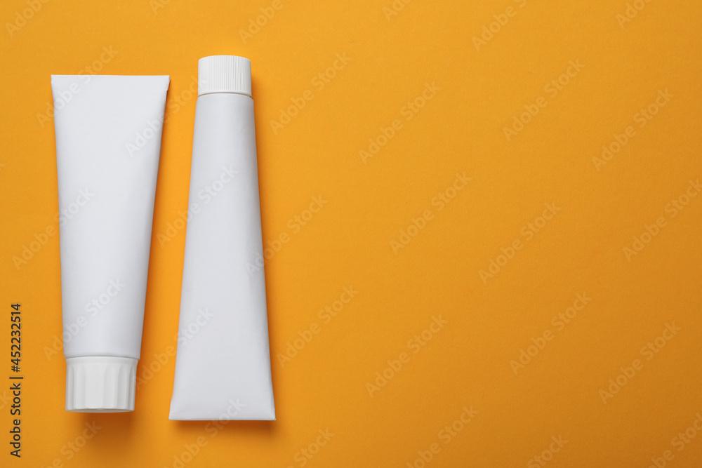 Blank tubes of toothpaste on orange background, flat lay. Space for text Blank tubes of toothpaste on orange background, flat lay. Space for text