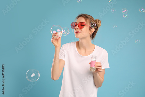 Young woman blowing soap bubbles on light blue background