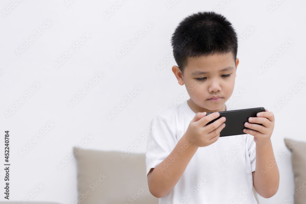 Little boy having fun playing game on mobile phone, Preschool kid sitting on sofa with smiling face watching cartoon on smartphone, Child using cell phone while relaxing at home Little boy having fun playing game on mobile phone, Preschool kid sitting on sofa with smiling face watching cartoon on smartphone, Child using cell phone while relaxing at home