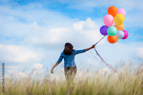 Woman holding balloons running on green meadow white cloud and blue sky with happiness Cheerful and relax. Hands holding vibrant air balloons play on birthday party happy times summer sunlight outdoor