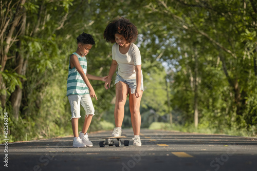 Childhood and leisure activity - African American curly hair children training skateboard togetherness on the road at park.