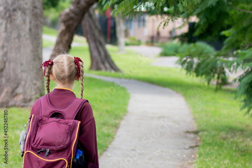 A girl wearing maroon school uniform walking to school alone. School students return to classrooms after COVID-19 outbreak
