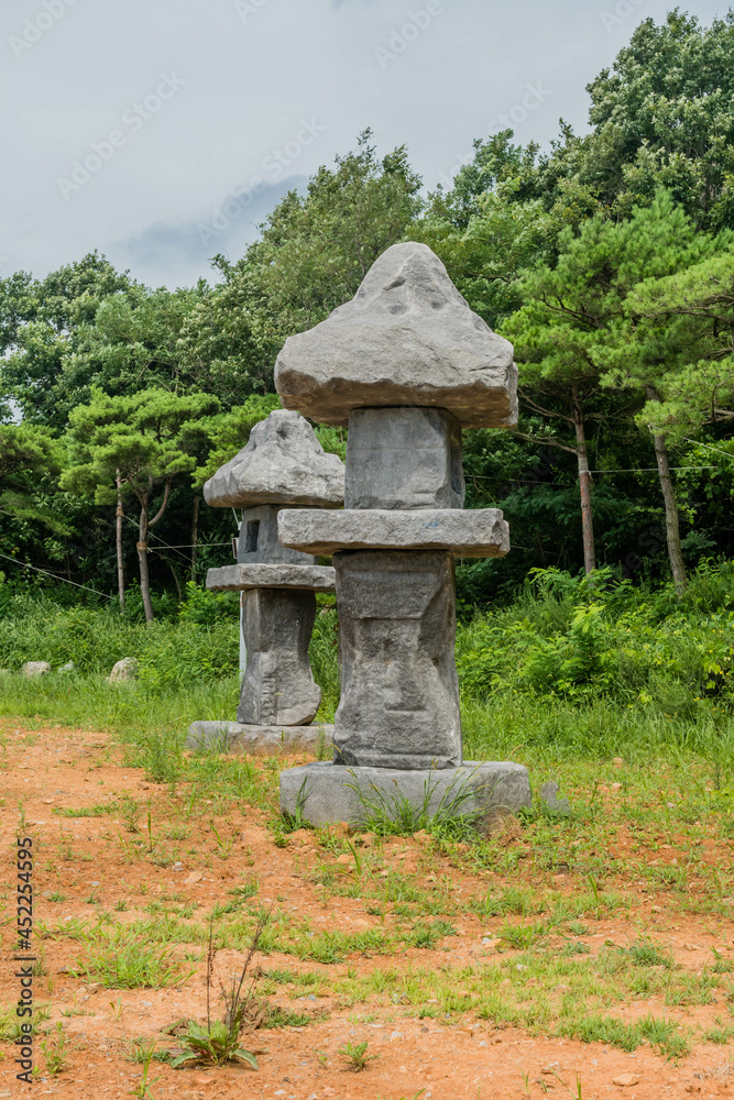 Side view of two large stone carved lanterns beside concrete walkway in rural public park. Side view of two large stone carved lanterns beside concrete walkway in rural public park.