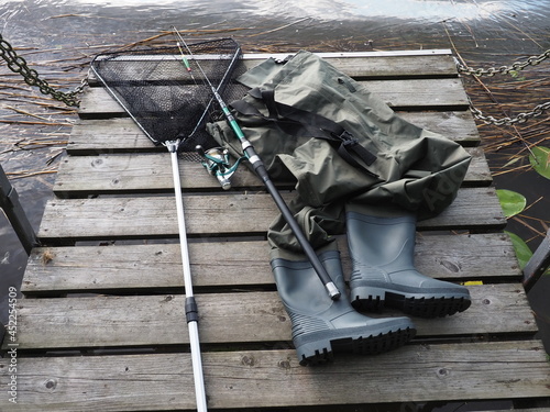 Chest waders, fish catch net and fishing rod. Hobby and spending time in nature. photo