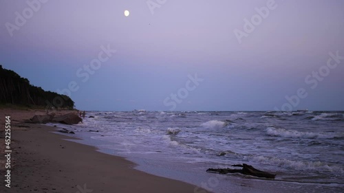 Baltic sea coast in the moonlight. A sea ship sailing in the distance from the port of Klaipeda and people walking on the sea shore. Holiday in Lithuania concept. 