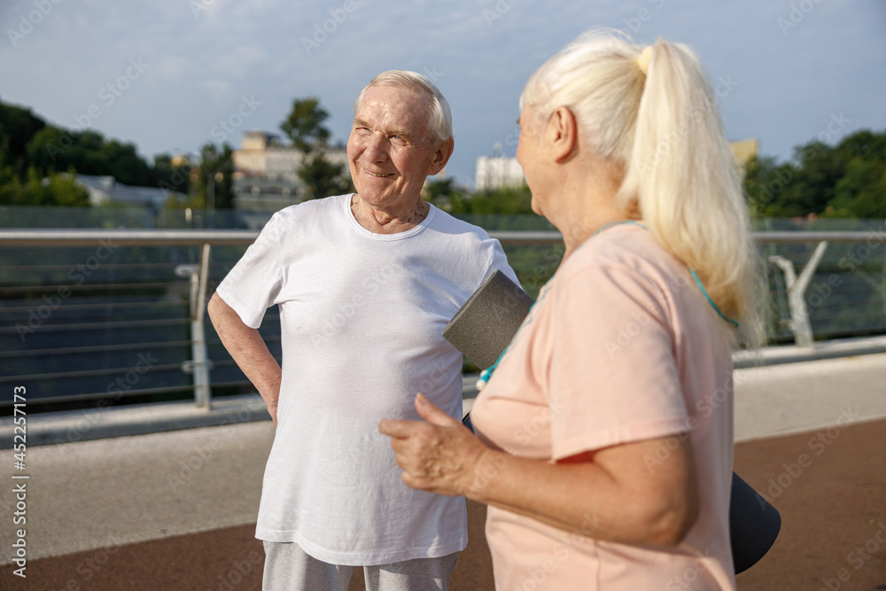 Happy senior man and wife with mat stand on footbridge at sunset