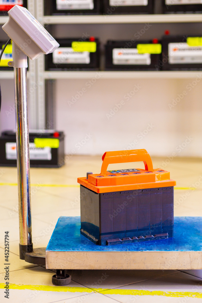 Car battery stands on floor scales against the background of a blurred rack Car battery stands on floor scales against the background of a blurred rack