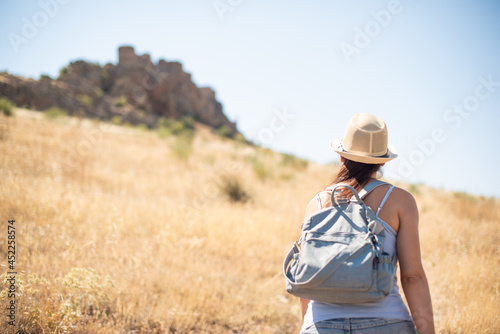 Woman in a hat walking through a field towards a castle on a hill