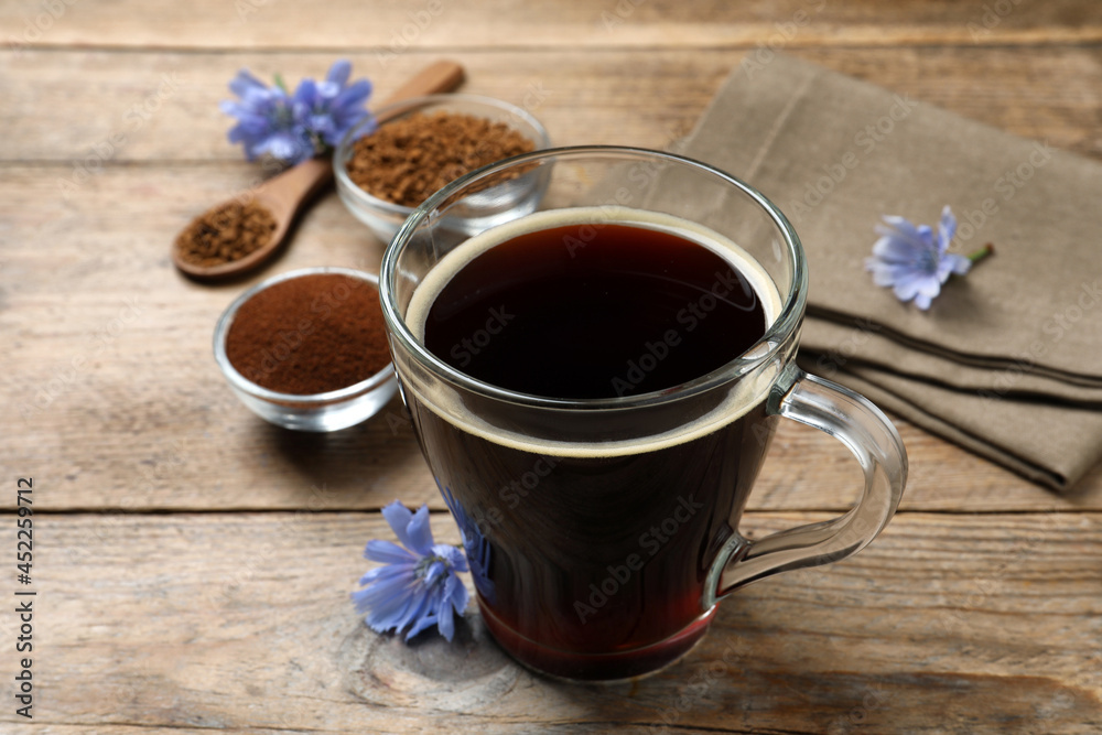 Glass cup of delicious chicory drink and flowers on wooden table, closeup Glass cup of delicious chicory drink and flowers on wooden table, closeup