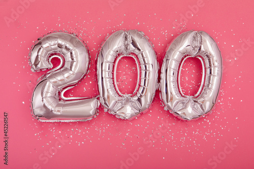From above of silver shiny balloons demonstrating number 200 on pink background with scattered glitter photo