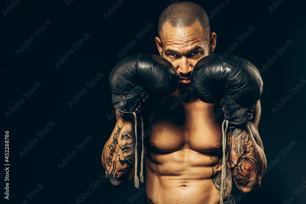 Fototapeta premium Studio portrait of a muscular boxer with a naked torso on a dark background. The Latin American puncher's attack. A serious fighter performs punches.
