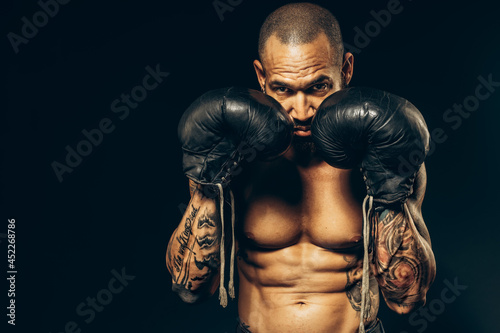 Studio portrait of a muscular boxer with a naked torso on a dark background. The Latin American puncher's attack. A serious fighter performs punches.