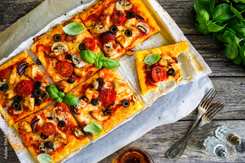 Pizza with white mushrooms, chicken nuggets, tomatoes, black olives and mozzarella on wooden background 