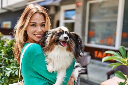 Young caucasian girl smiling happy holding dog at the city.