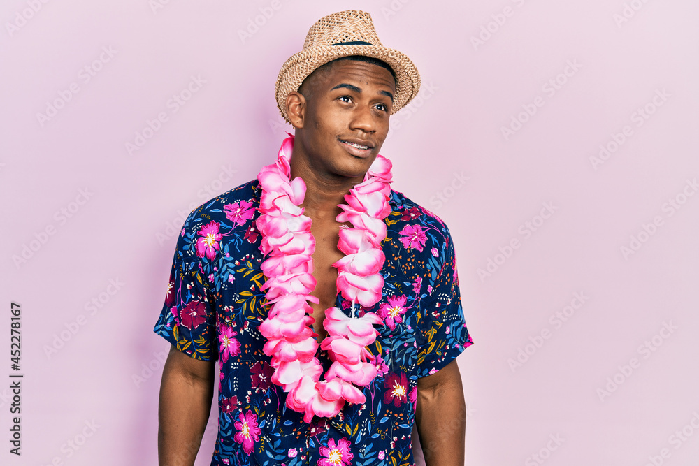 Young black man wearing summer shirt and hawaiian lei looking away to side with smile on face, natural expression. laughing confident.