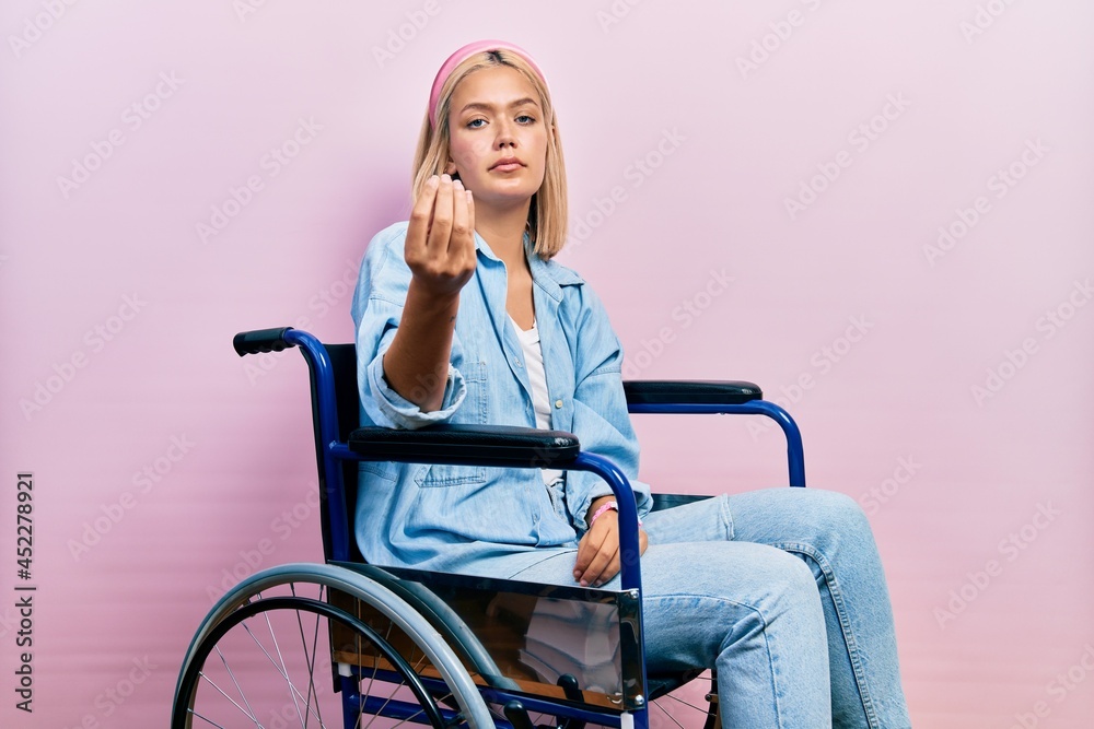 Beautiful blonde woman sitting on wheelchair doing italian gesture with hand and fingers confident expression Beautiful blonde woman sitting on wheelchair doing italian gesture with hand and fingers confident expression