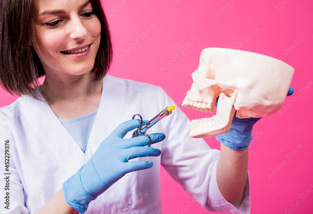 Woman dentist with a carpool syringe injects anesthetic into the gum of the artificial skull Woman dentist with a carpool syringe injects anesthetic into the gum of the artificial skull