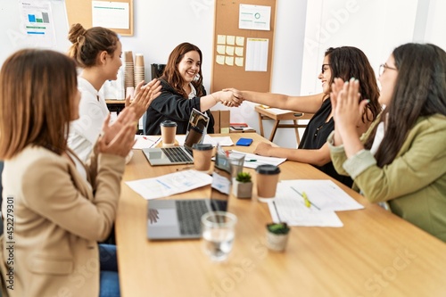 Group of businesswomen smiling and clapping to partners handshake at the office.